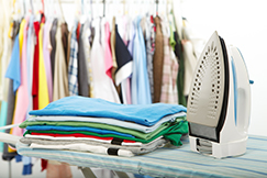 Pile of clothes with clothes on coat rail behind. Iron in the foreground